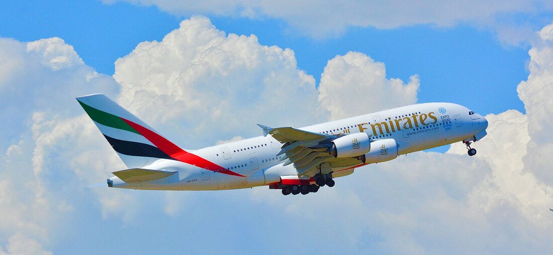 An Emirates Airbus A380 climbing against cumulus cloud, its full-length double-deck fuselage clearly visible