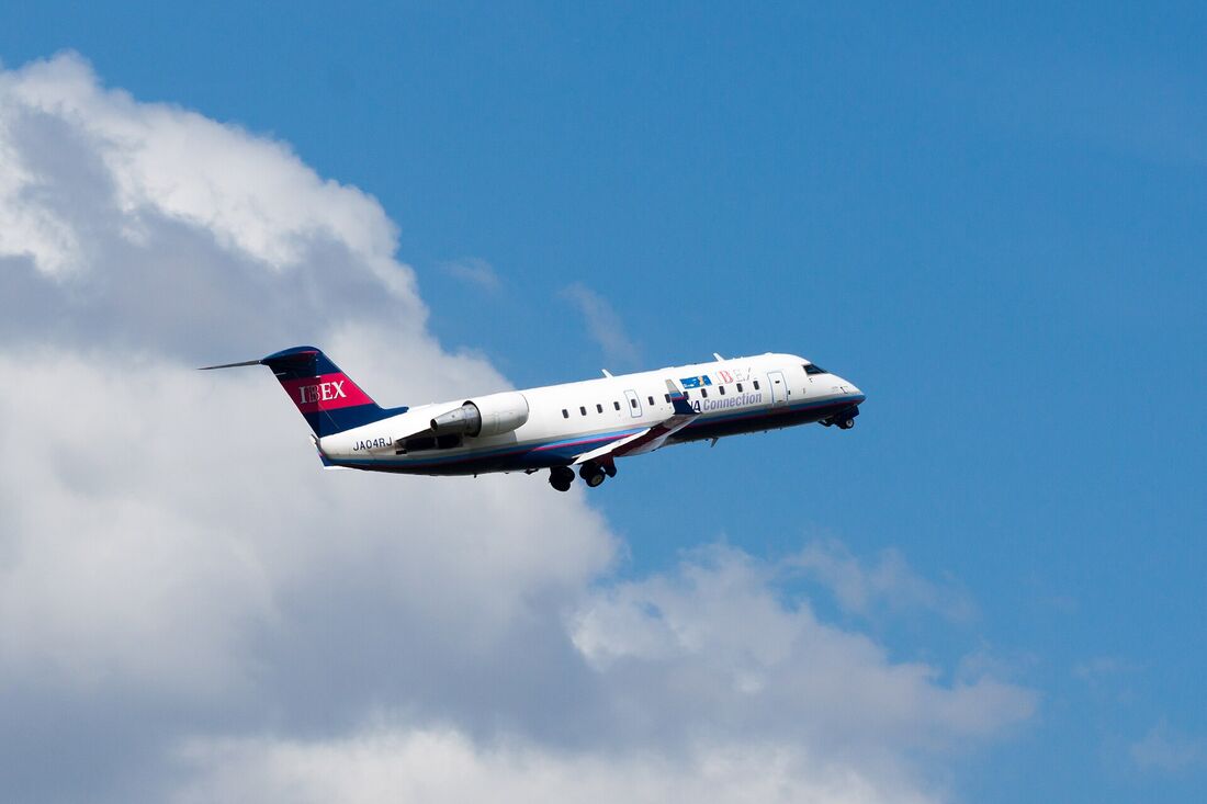 A Bombardier CRJ-200 regional jet climbing against blue sky, showing its T-tail and rear-fuselage mounted engines